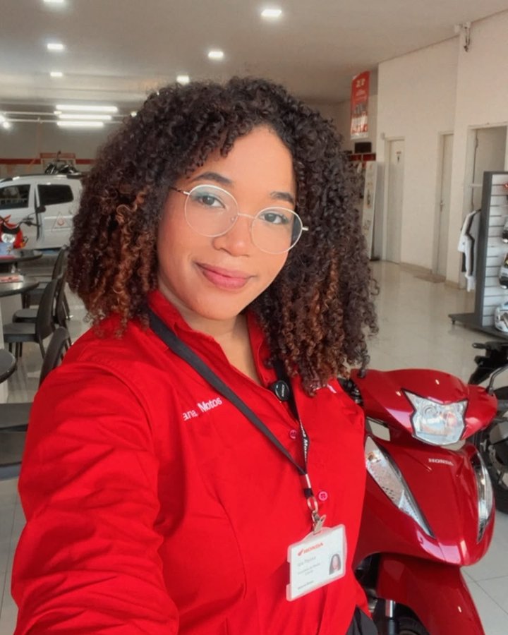 Yara, consultora de vendas Honda, na loja ao lado de uma Honda POP 110i vermelha
